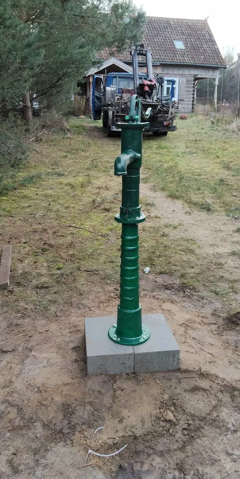 Zielona żeliwna pompa ręczna na betonowym cokole na trawniku